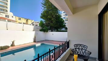 A balcony with a swimming pool, a book, and a glass of juice.