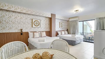 A hotel room with two beds, a dining area with wicker chairs, and a balcony with a view.