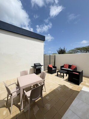 Eine Terrasse mit Tisch und Stühlen, einem Grill und einer Sitzecke.