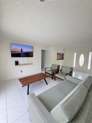 A living room with a flat-screen TV, a wooden coffee table, a sofa, and two armchairs. - Dushi Aruba 3BDR-Villa - Private Pool •-Central Location - (Piedra Plat)