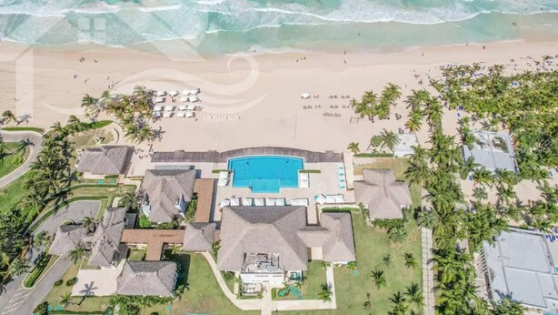 Vista aerea di un resort con piscina, spiaggia e palme.