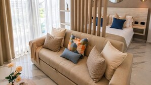 Une chambre d’hôtel moderne avec un canapé, un lit avec des oreillers, un miroir, une cloison en bois et une petite table sur laquelle est posé un vase.