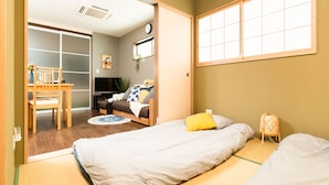 A room with tatami flooring, a futon bed, a small table with a chair, a TV, and a sliding door leading to another room. - ODA VILLA@Namba (Osaka City)