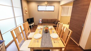 A dining area with a wooden table, chairs, and a TV in the background. - ODA VILLA@Namba (Osaka City)