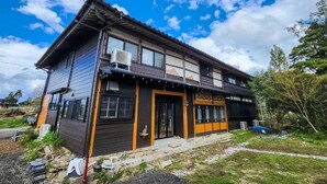A two-story building with a traditional architectural style, featuring a dark wooden exterior, a tiled roof, and large windows. - taipi house  (Sado)