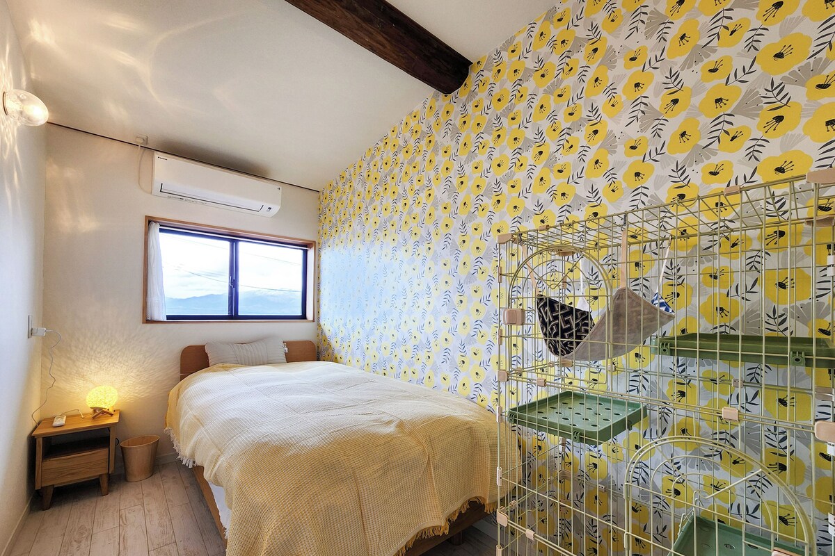 A room with a bed, a window, an air conditioning unit, a bedside lamp, and a wall with a floral pattern.