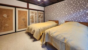A room with two beds, wooden ceiling beams, and artwork on the walls. - taipi house  (Sado)