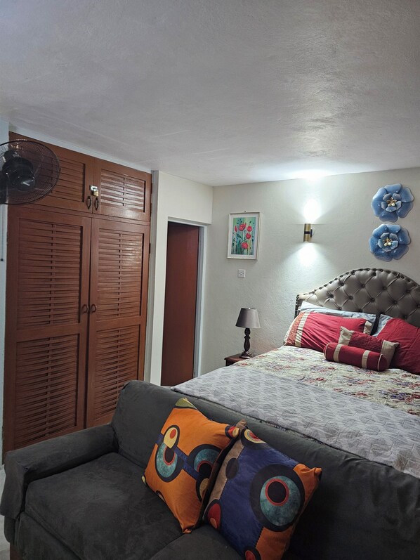 A bedroom with a bed, a couch, a wardrobe, and a wall with a flower decoration.