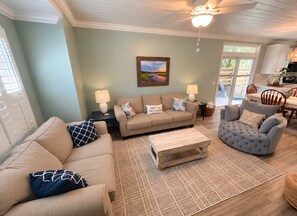 A living room with a sofa, armchair, coffee table, and a painting on the wall. - Coastal Retreat on Beachview | Walk to Beach, Village + Family-Friendly Stay (Saint Simons Island)
