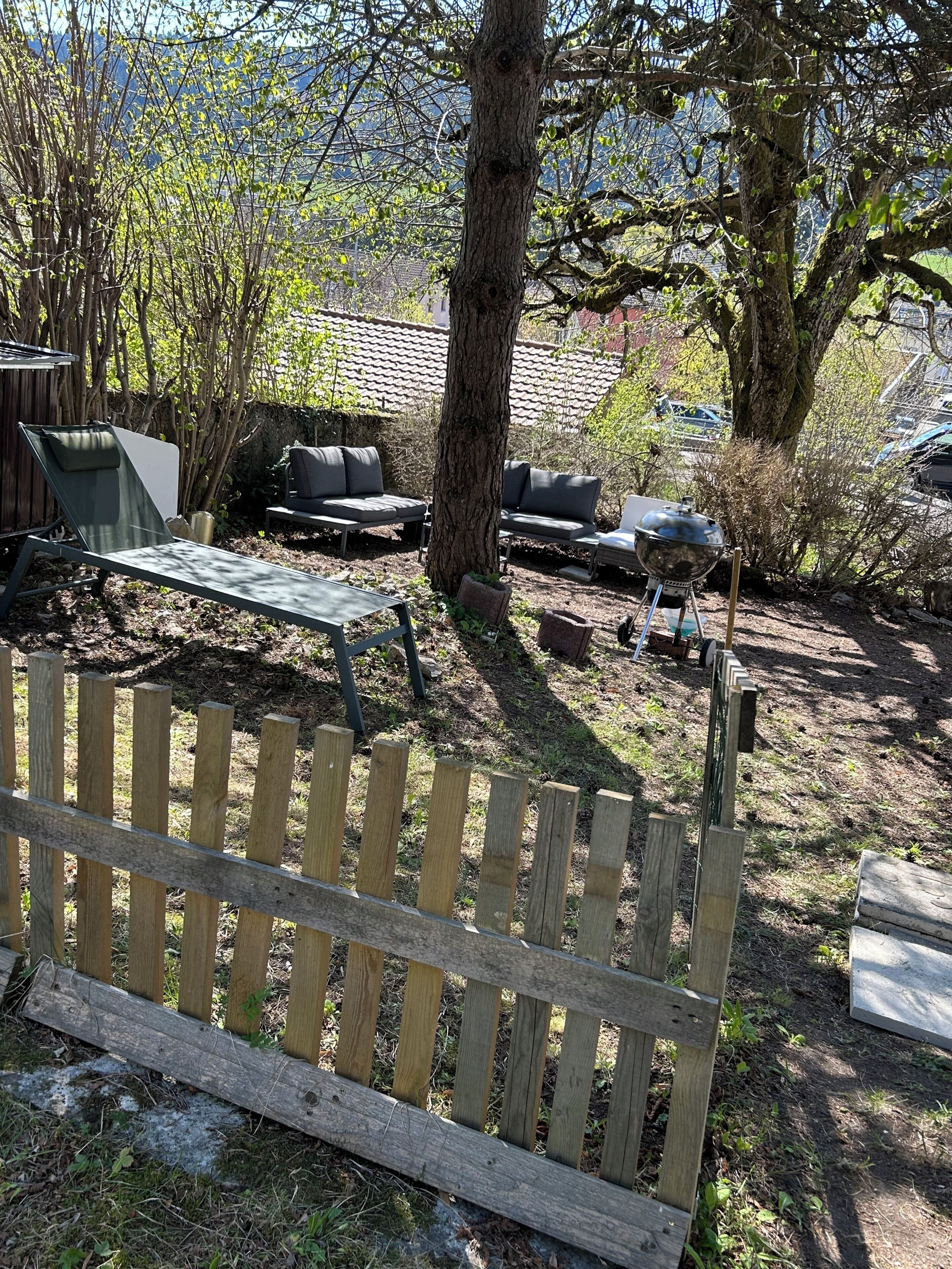 A wooden fence, a metal grill, and outdoor furniture in a backyard setting.