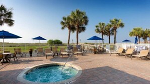 A pool area with lounge chairs and umbrellas, surrounded by palm trees and a fence. - Cozy 2-bedroom condo in amazing North Myrtle Beach with AC (North Myrtle Beach)