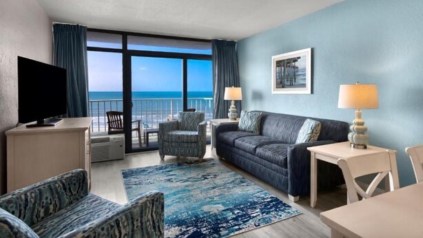 A hotel room with a balcony, a sofa, a chair, a TV, and a table. - Cozy 2-bedroom condo in amazing North Myrtle Beach with AC (North Myrtle Beach)