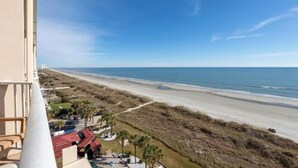 A beachfront view from a balcony with a clear sky, sandy beach, and sparse vegetation. - Cozy 2-bedroom condo in amazing North Myrtle Beach with AC (North Myrtle Beach)