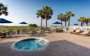 Un espace piscine aménagé avec des chaises longues, des parasols et des palmiers.