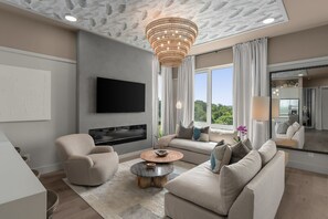 Ein modernes Wohnzimmer mit Flachbildfernseher, Kamin, großem Fenster mit Vorhängen und einer Kristallleuchter.
