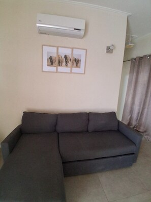 A living room with a sectional sofa, an air conditioner, and a framed picture on the wall. - Cozy 1-bedroom apartment in fabulous Mullins, St. Peter with air conditioning! (Saint. Peter)