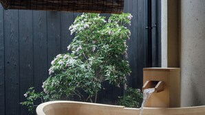 Une baignoire en bois remplie d’eau, une structure en bois et un arbre aux fleurs roses.