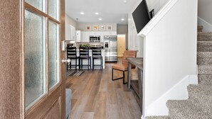 Una cocina moderna con armarios blancos, un refrigerador de acero inoxidable y una zona de comedor con una mesa y sillas de madera.