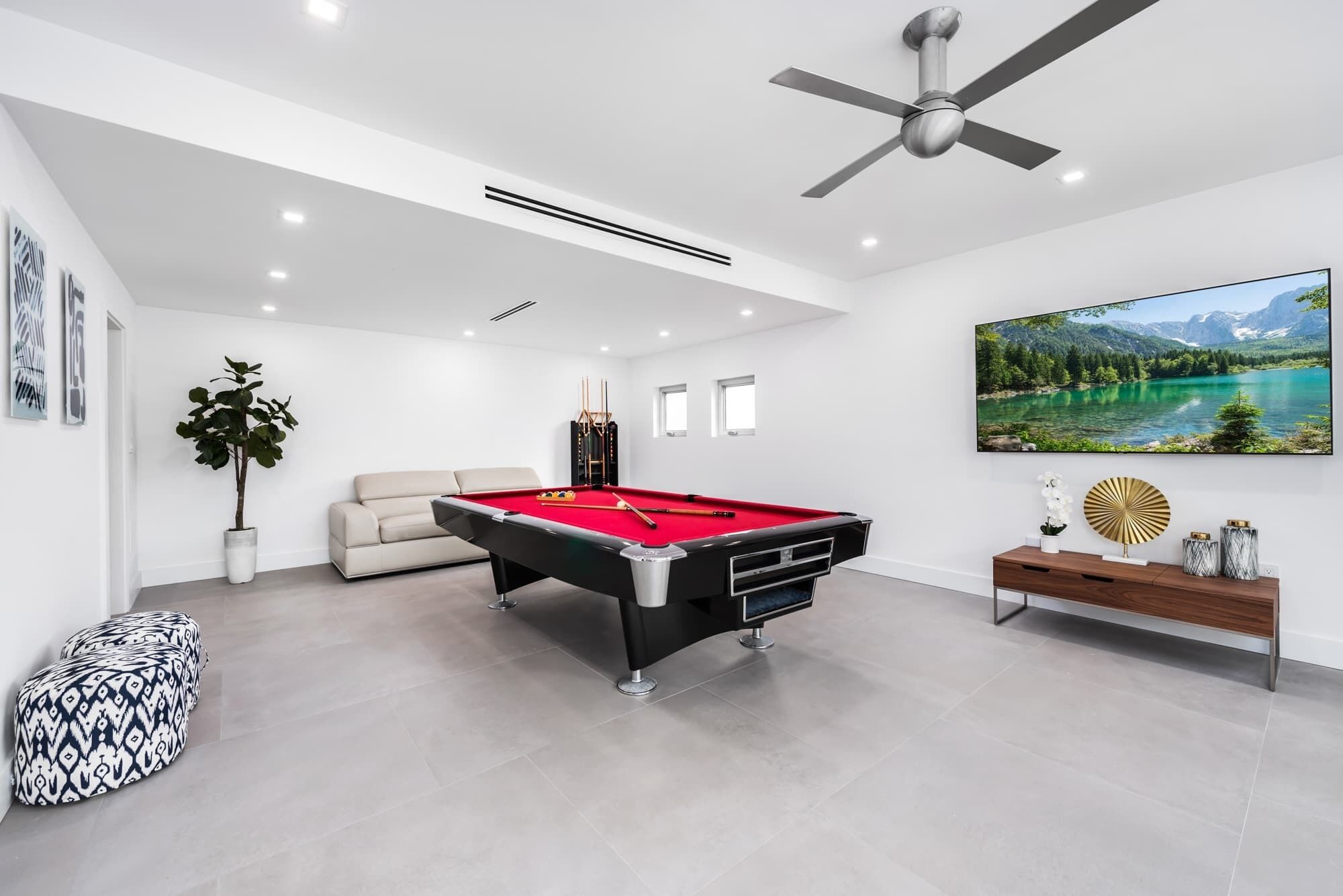 Un salon moderne avec une table de billard, un canapé, un ventilateur de plafond et un grand tableau représentant un paysage.