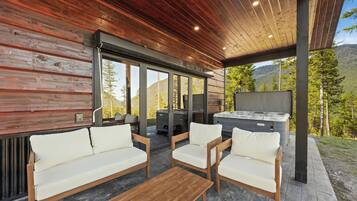 A covered outdoor seating area with wooden furniture, a hot tub, and a view of a mountainous landscape.