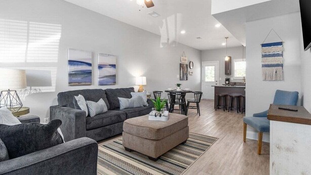 A modern living room with a grey sofa, a coffee table, and a ceiling fan. There is a kitchen area with a bar and stools. - 19th Hole Haven in Sango 1625 Golf Club, #601 (Clarksville)