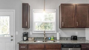 A kitchen with dark wooden cabinets, a stainless steel dishwasher, a granite countertop, and a window with blinds. - 19th Hole Haven in Sango 1625 Golf Club, #601 (Clarksville)