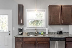 A kitchen with a dishwasher, a coffee maker, and a window with blinds.