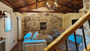 Un intérieur rustique avec un mur en pierre, un plafond en bois, un canapé et un escalier.