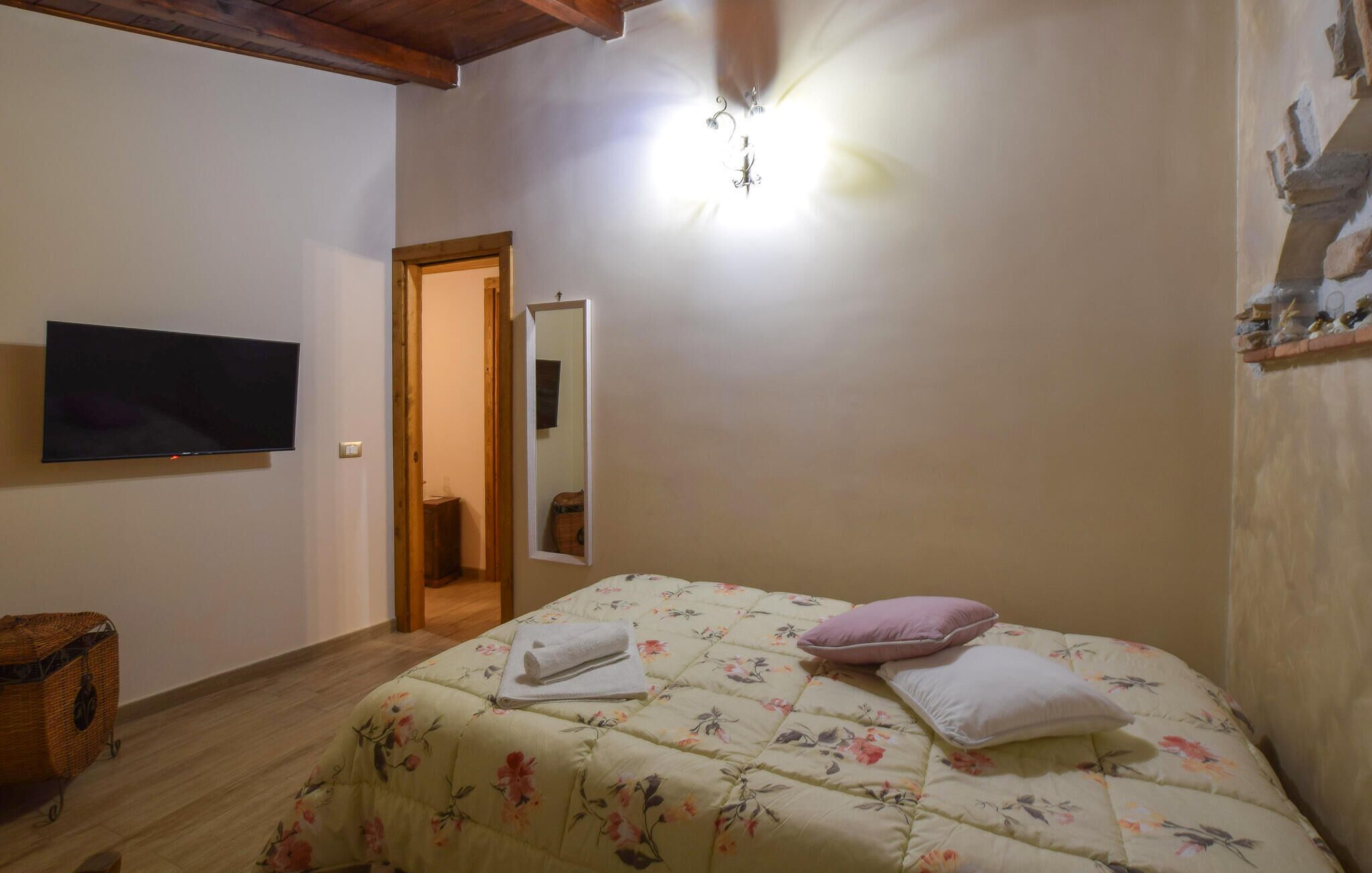 A bedroom with a bed, a television, a wooden floor, and a door leading to another room.