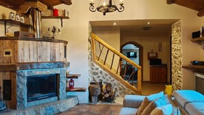 Un intérieur rustique avec une cheminée en pierre, des poutres en bois, un escalier et un coin salon confortable.