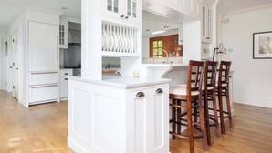 A kitchen with white cabinetry, a marble countertop, and wooden chairs. - Summerset Villa by Rove - Family Home With Pool & Hot Tub (Bridgehampton)