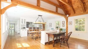 A spacious kitchen with wooden beams, a dining area with a large island, and a view of the outdoors. - Summerset Villa by Rove - Family Home With Pool & Hot Tub (Bridgehampton)