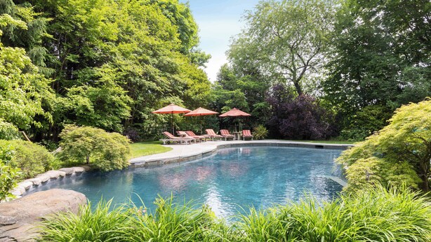 A swimming pool with lounge chairs and umbrellas, surrounded by lush greenery. - Summerset Villa by Rove - Family Home With Pool & Hot Tub (Bridgehampton)