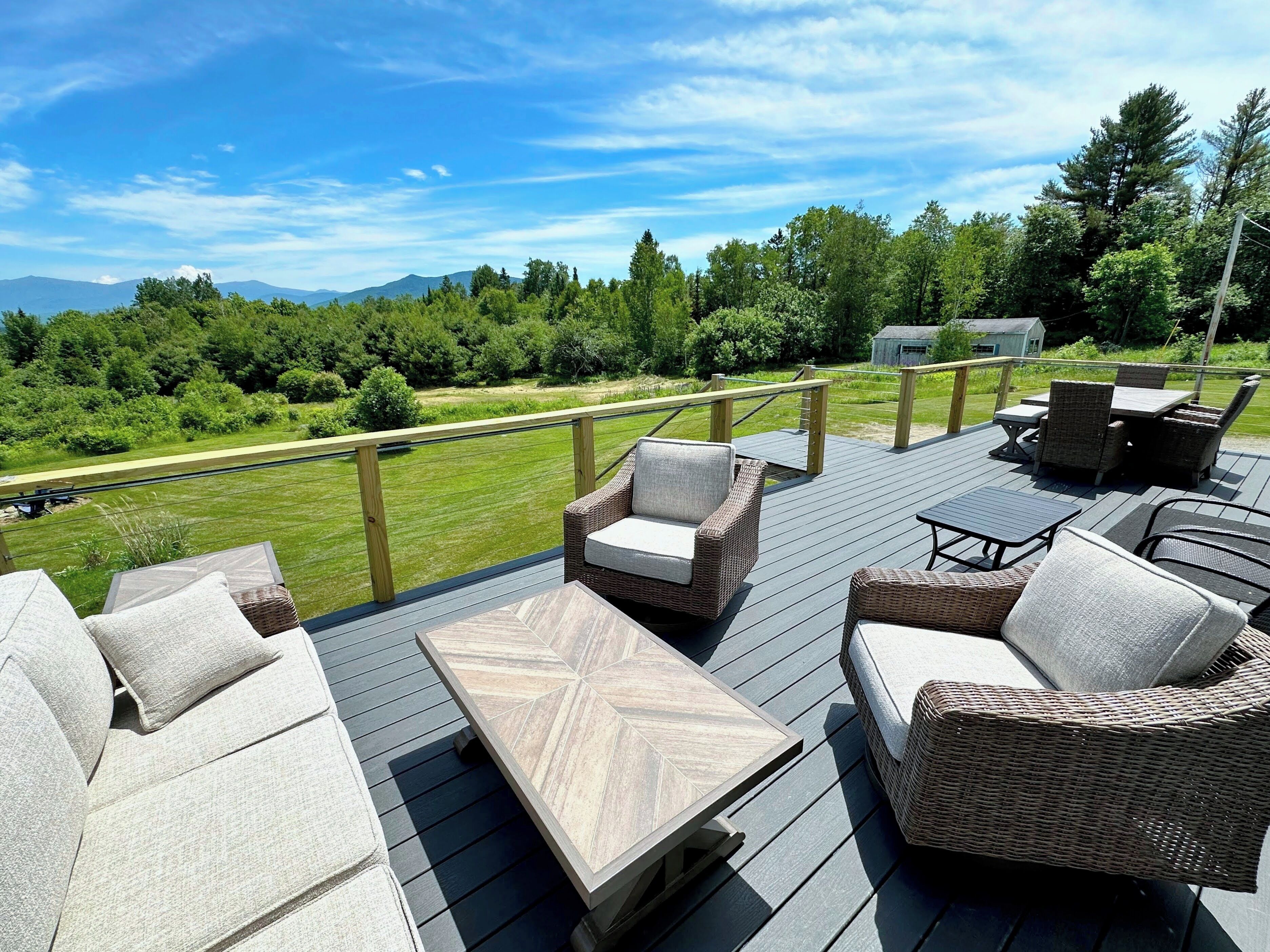A deck with outdoor furniture, a view of a green landscape, and a wooden railing.