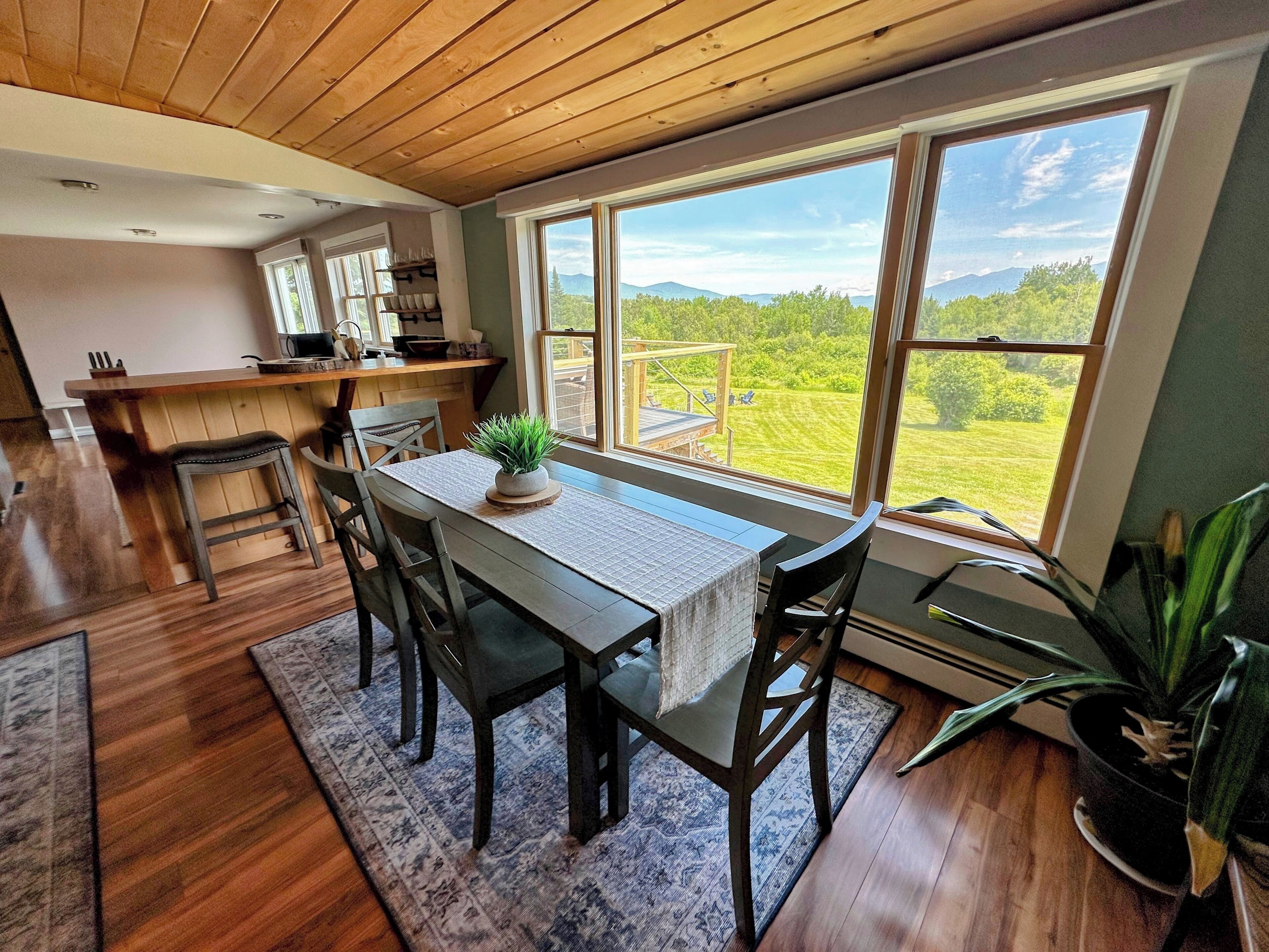 Un comedor con una mesa, sillas y vistas a un paisaje verde a través de amplios ventanales.