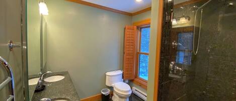 Une salle de bain avec deux lavabos, des toilettes et une douche.