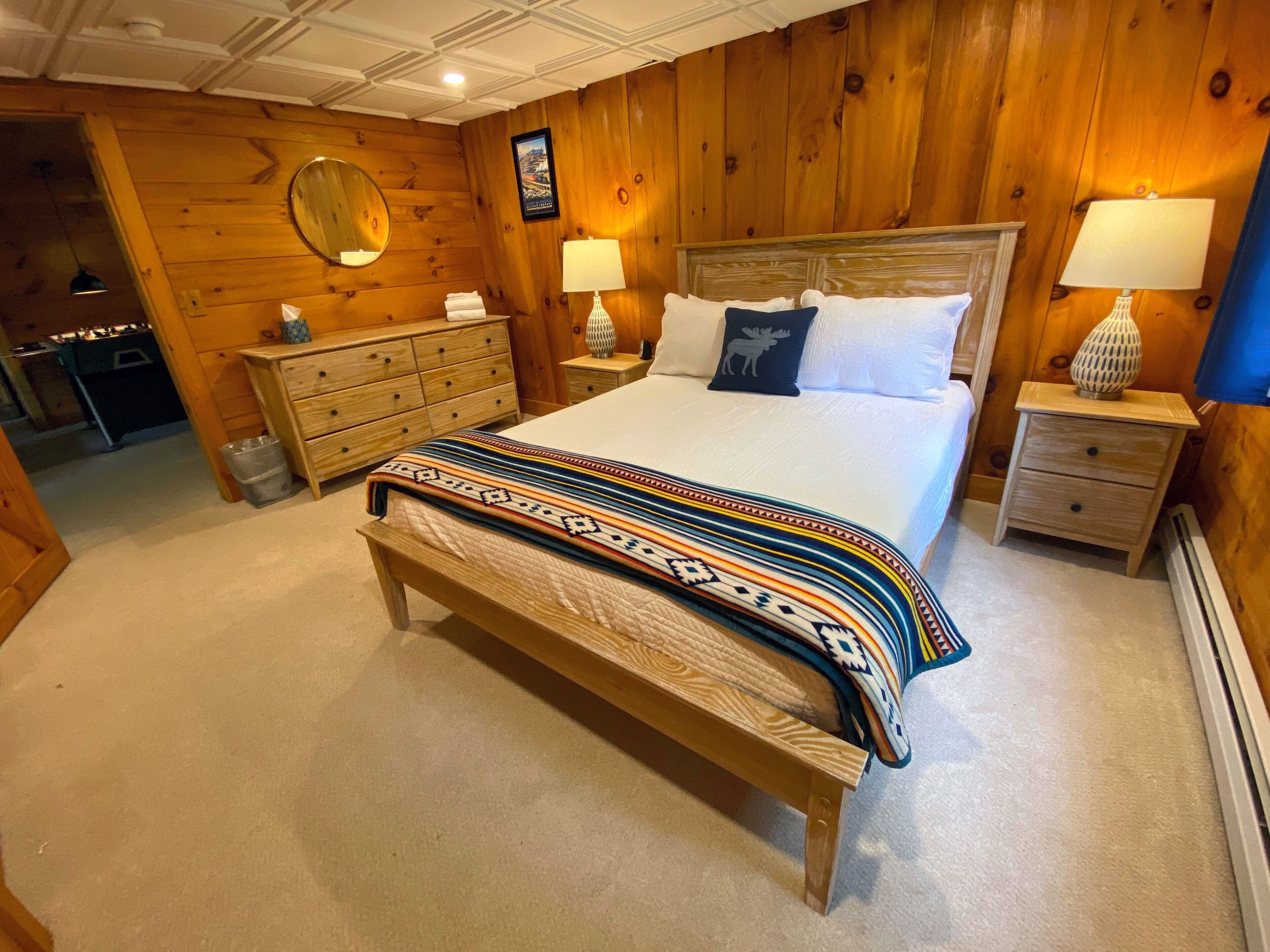 Ein Schlafzimmer mit Holzwänden, einem Bett, Nachttischen, einer Kommode und einem Spiegel.