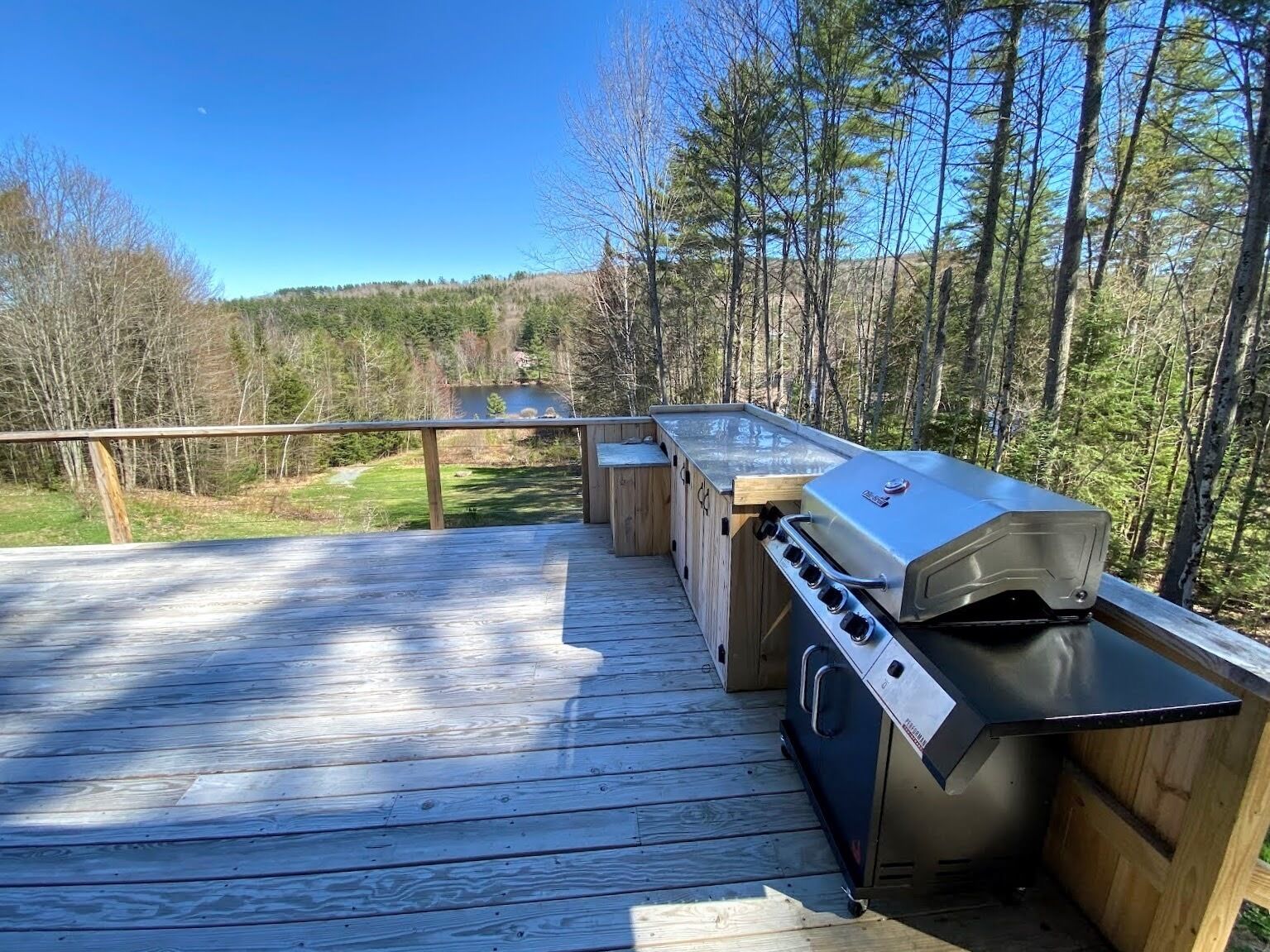 Una terrazza esterna con una griglia barbecue, panche in legno e vista su una zona boschiva.