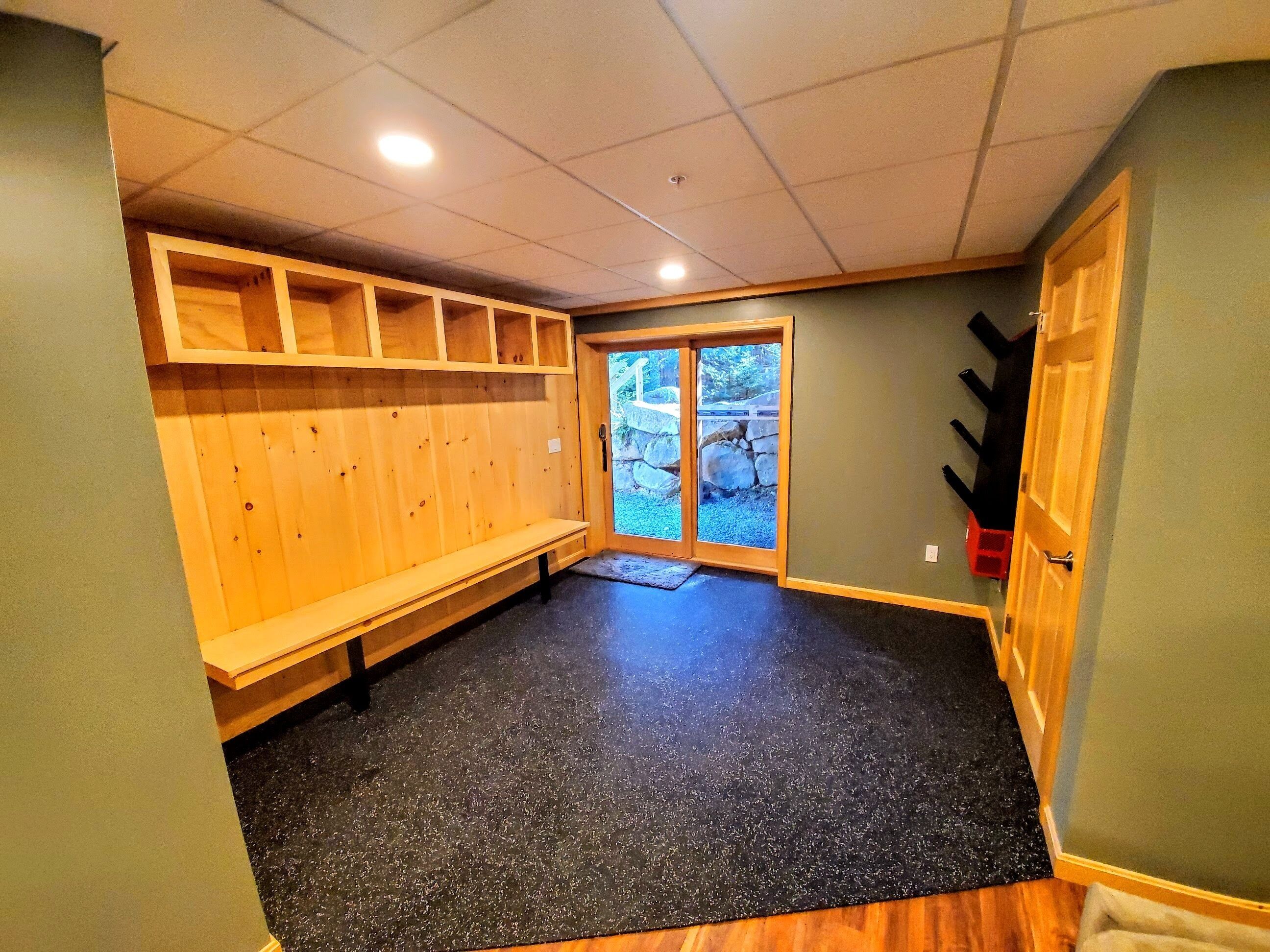 Una habitación con un banco, estanterías de madera, una puerta que da al exterior y un suelo con motas negras.
