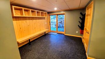 Una habitación con un banco, estanterías de madera, una puerta que da al exterior y un suelo con motas negras.