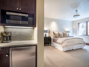 A modern kitchen with a built-in oven, a coffee maker, and a refrigerator. The bedroom features a large bed with a headboard, a nightstand, and a window with a view.