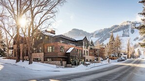 A modern multi-story building with large windows, a brick facade, and a snow-covered landscape with mountains in the background.