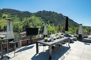 An outdoor terrace with a table, chairs, a flat-screen TV, and decorative plants.