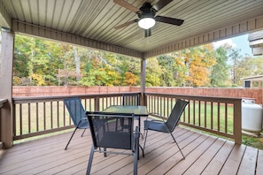 Une terrasse couverte avec une table et des chaises, un ventilateur de plafond et une vue sur les arbres.