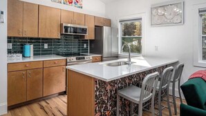 A modern kitchen with wooden cabinets, a stainless steel refrigerator, a microwave, and a coffee station. - Full Bloom Tree House - Stonewall Road (Pittsboro)