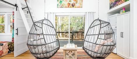 Una habitación con dos sillones colgantes tipo huevo, un tapete colorido, un armario blanco y un cuadro en la pared.