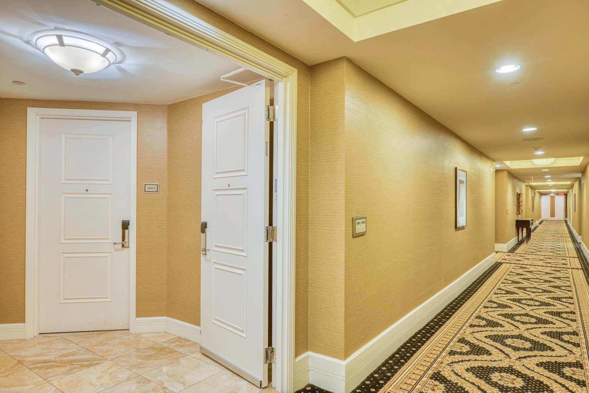 A hotel hallway with two white doors, beige walls, and patterned carpet.