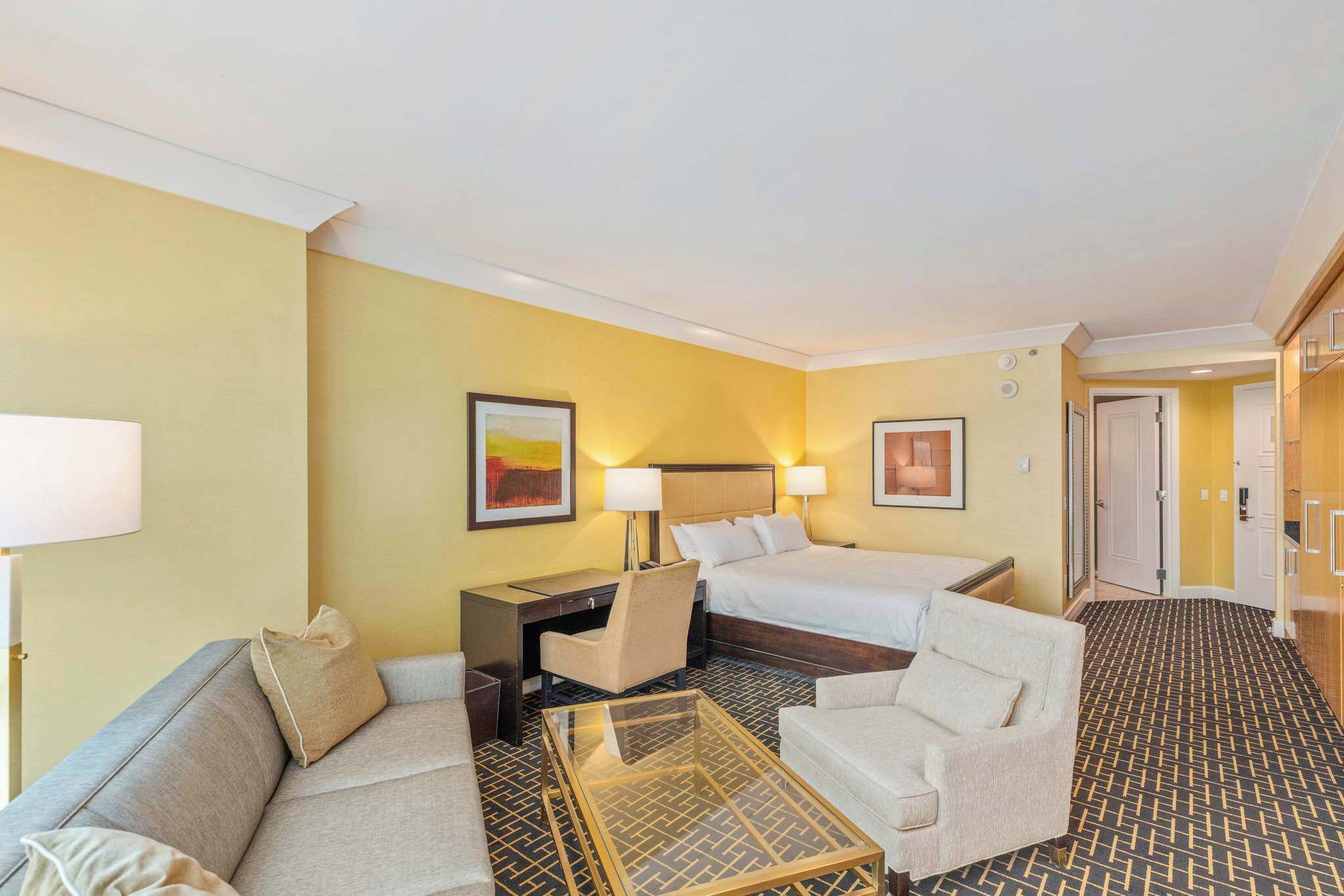 Ein Hotelzimmer mit einer Couch, zwei Einzelbetten, einem Schreibtisch, einem Stuhl und einem Couchtisch.