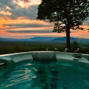 A hot tub with a mountain view, surrounded by lounge chairs.