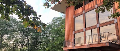 A modern two-story building with a balcony, surrounded by trees and a sunset view.